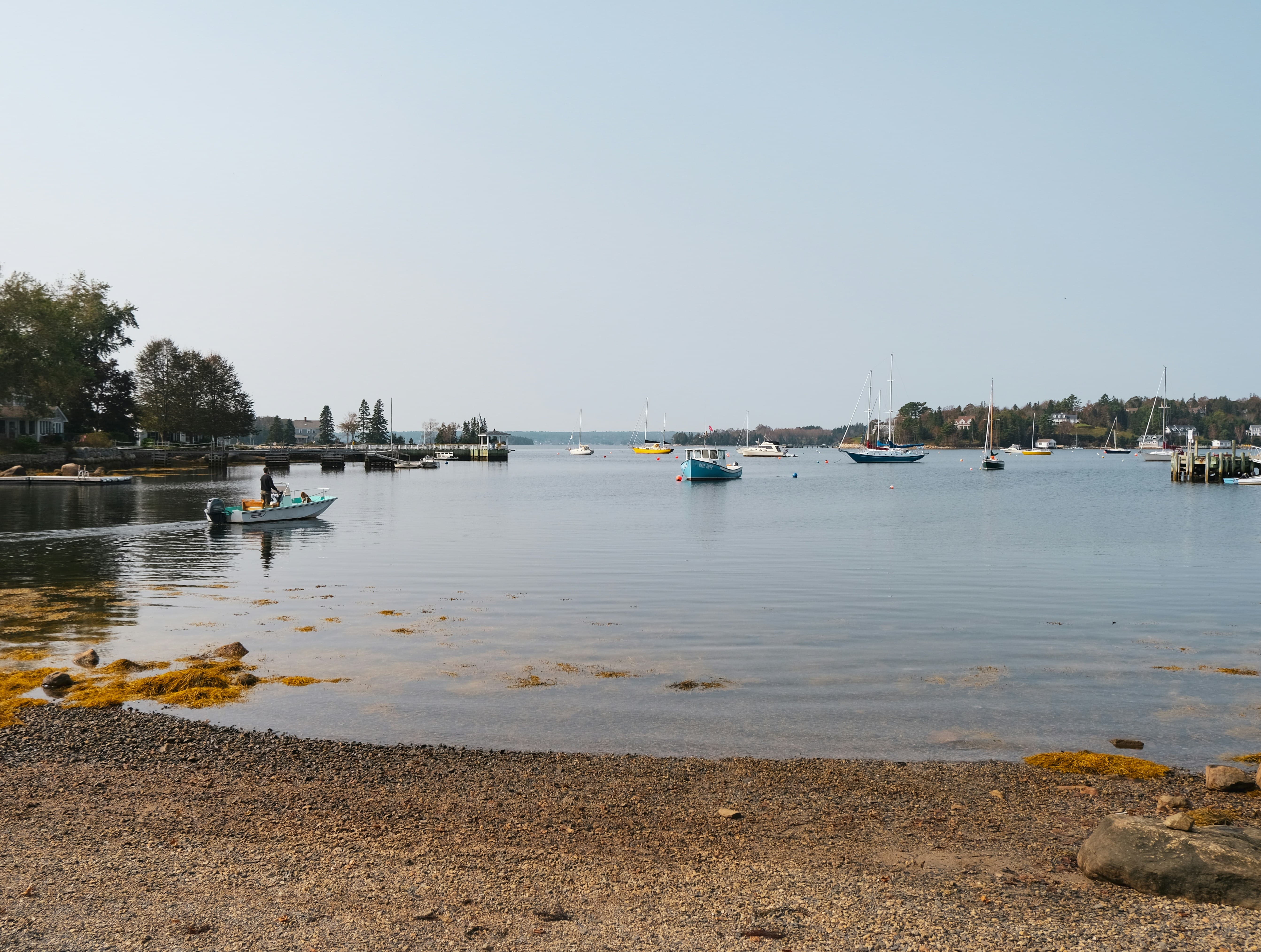 Photograph taken from a beach looking out at a busy harbour filled with sailboats and docks.